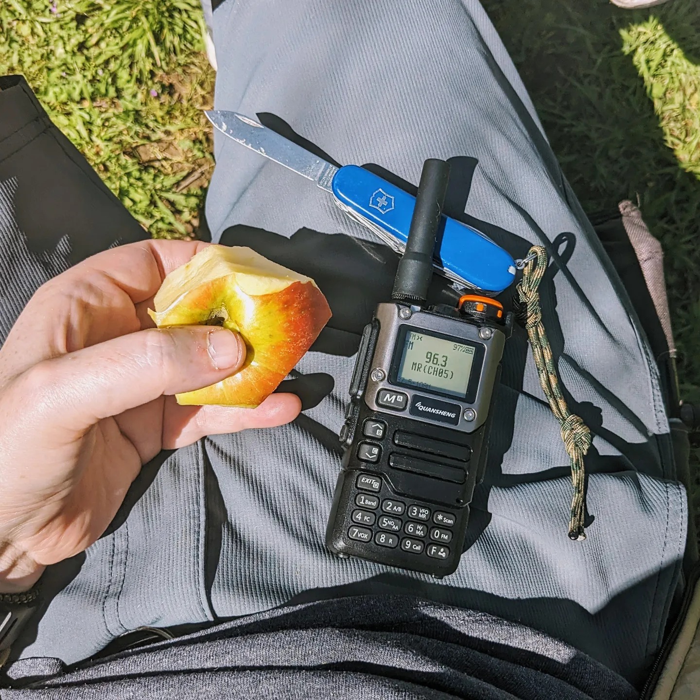 A photo of a lap with an apple, a pocket knife, and a ham radio tuned to a local FM broadcast station